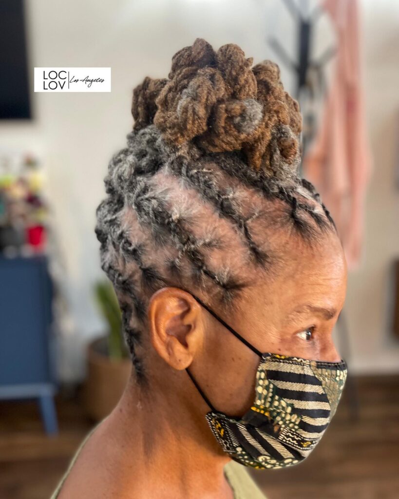 A side view of a woman over 60 with her salt-and-pepper locs styled into a high, voluminous, sculpted bun.