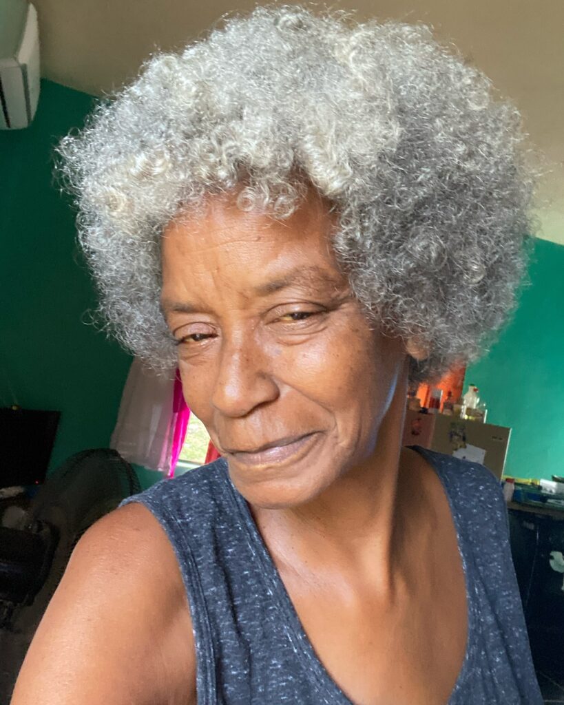 A woman with a rounded medium-length natural afro featuring a mix of gray and bright silver curls.