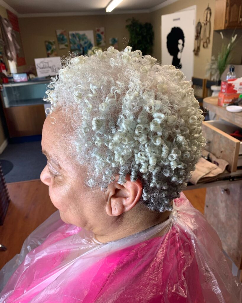 A side profile of a woman over 60 with short, tight spiral curls in a bright, icy white shade.