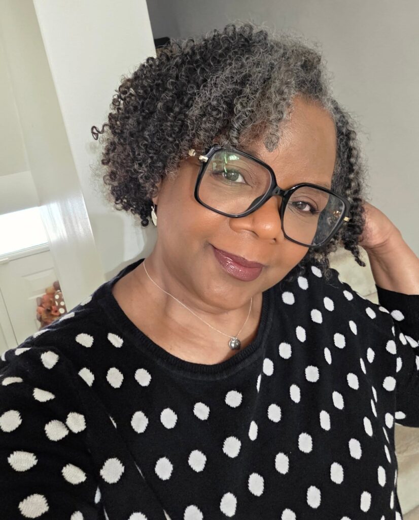 A woman with a chin-length salt-and-pepper natural curly bob, featuring a deep side part.
