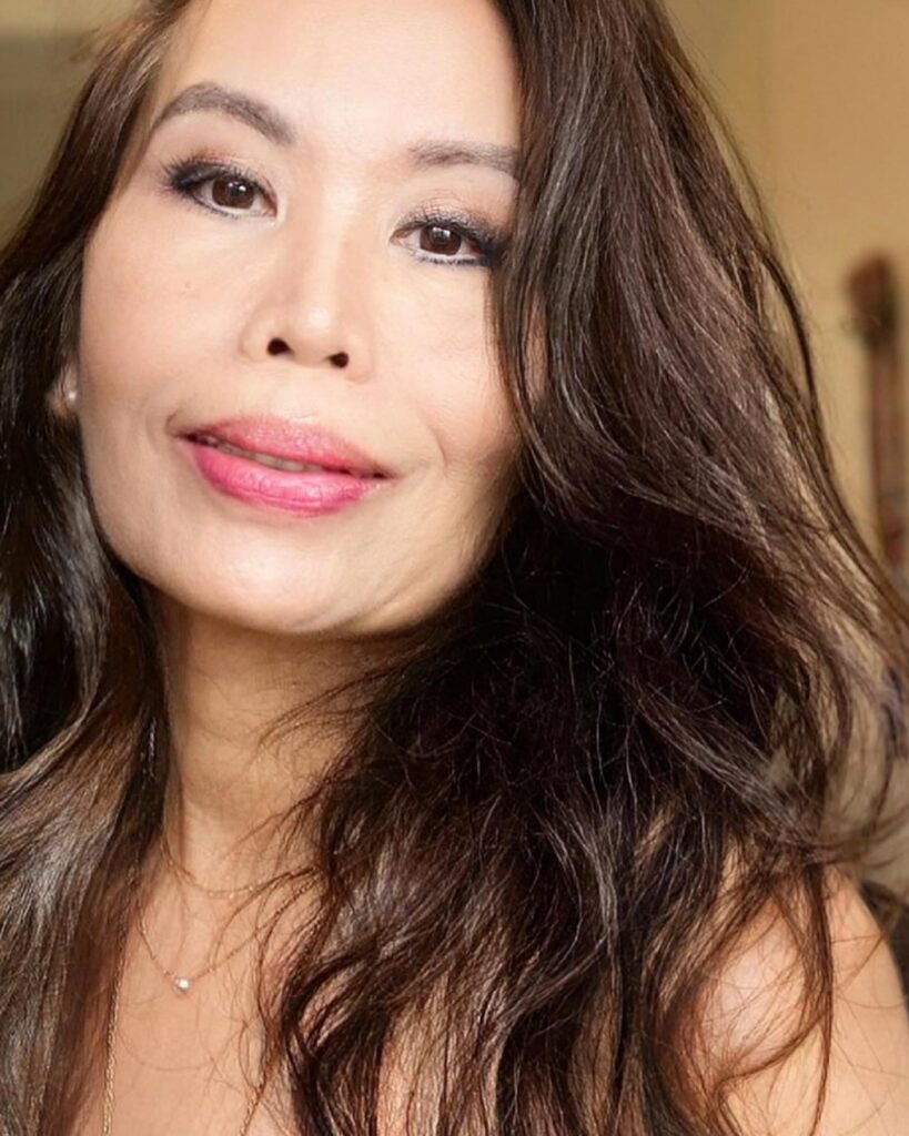 A woman over 60 with long dark brown hair styled in voluminous soft waves and layers.
