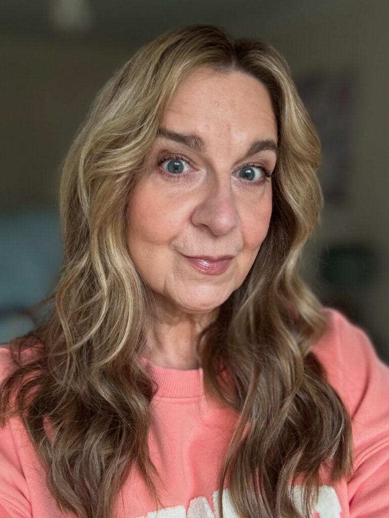 A woman over 60 with long wavy hair featuring a dark base and honey-blonde highlights.