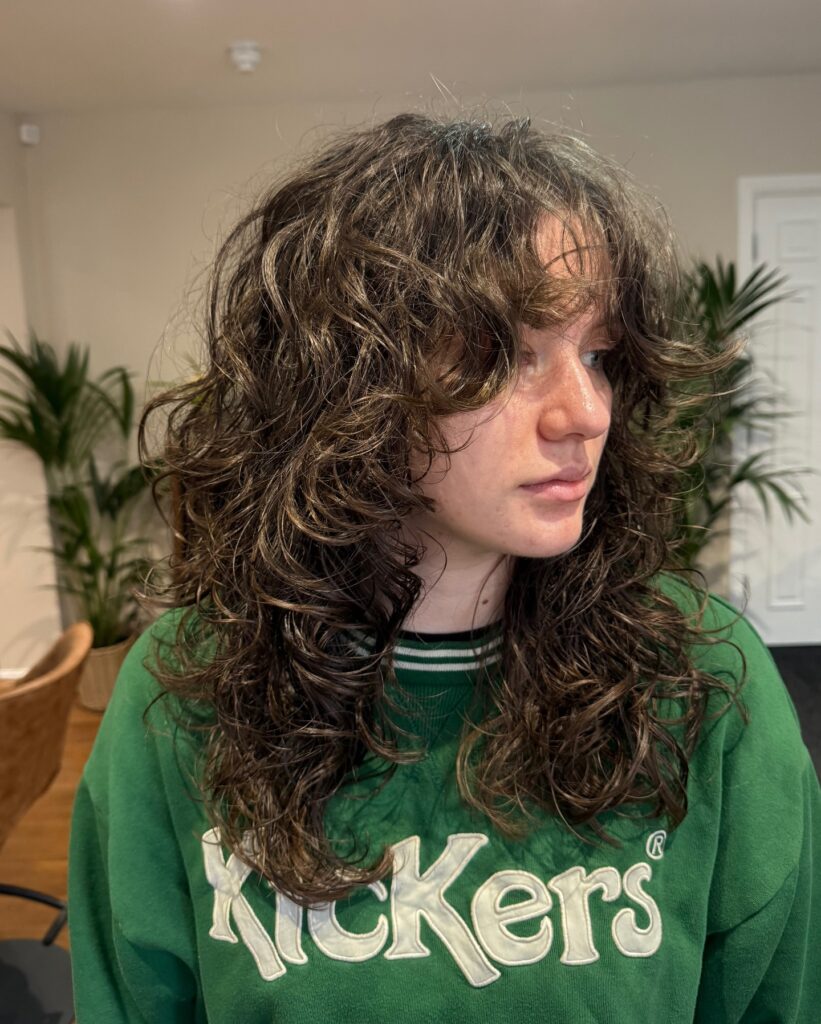 A young woman wearing a green sweatshirt with a messy dark brown shoulder-length choppy bob hairstyle featuring voluminous wavy layers and soft curtain bangs.