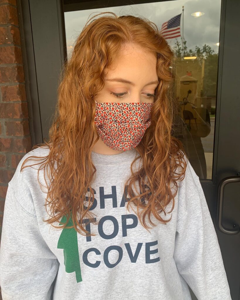 A woman with a strawberry blonde shoulder-length choppy bob hairstyle featuring loose waves and long face-framing curtain layers.
