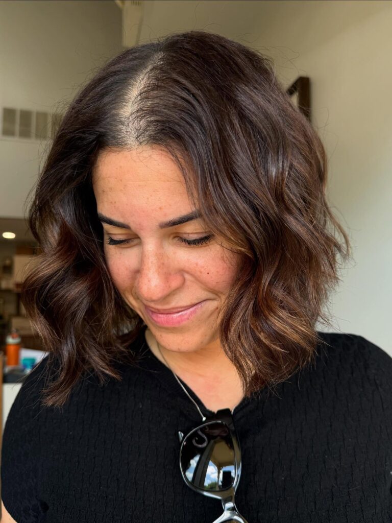 A woman looking down with a center-parted, shoulder-length chocolate brown choppy bob hairstyle styled in soft glossy waves.