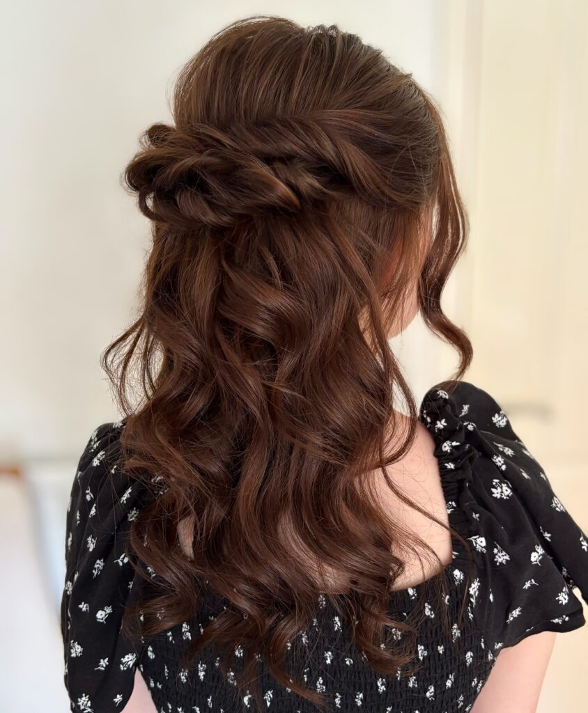 A back and side view of a woman with a chestnut brown long choppy bob hairstyle styled into a twisted half-up look with elegant waves and a face-framing tendril.