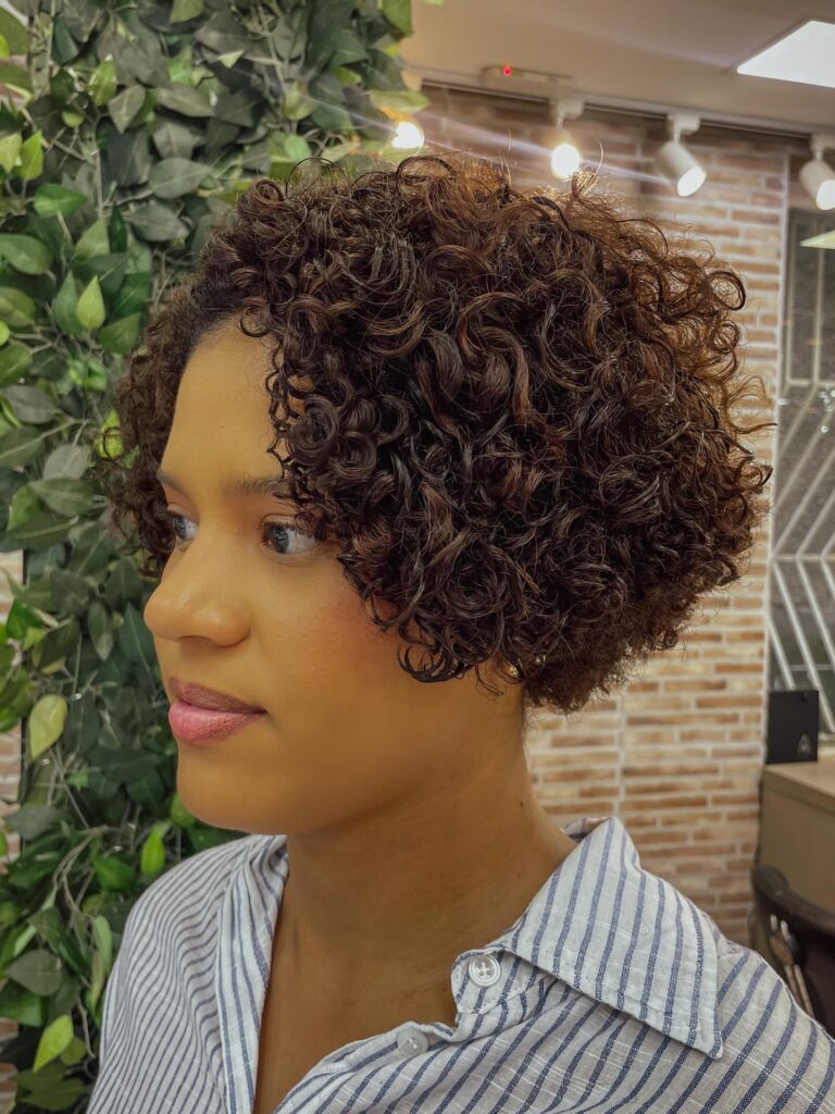 A woman with an ear-length curly bob in deep chocolate brunette, featuring tight corkscrew curls and a subtle side part.