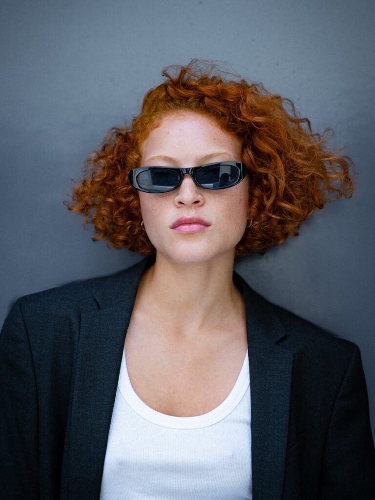 A woman with a vibrant copper curly bob styled with a messy side part and voluminous texture.