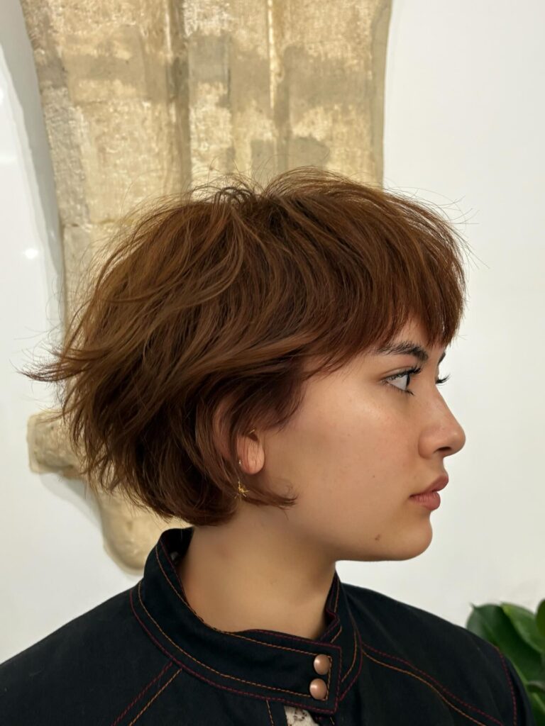 A tousled auburn layered bob with wispy bangs and soft textured volume.