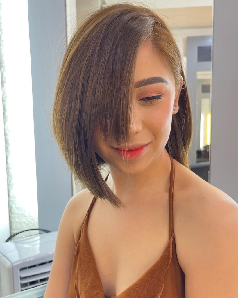 Straight angled bob with a long side fringe and smooth brunette layers framing the face.