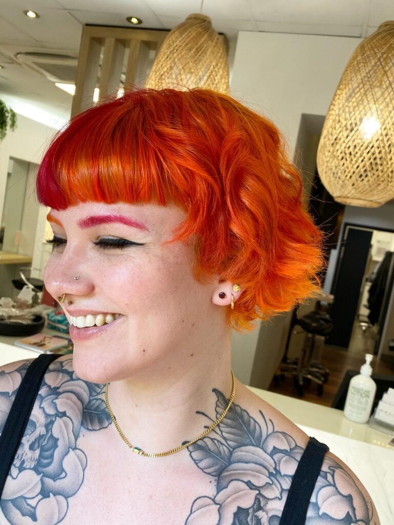 Bright orange layered bob with choppy texture and bold micro bangs.
