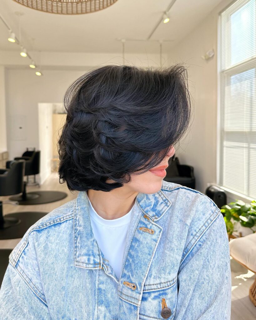 A voluminous dark layered bob with side-swept bangs and rounded textured layers.