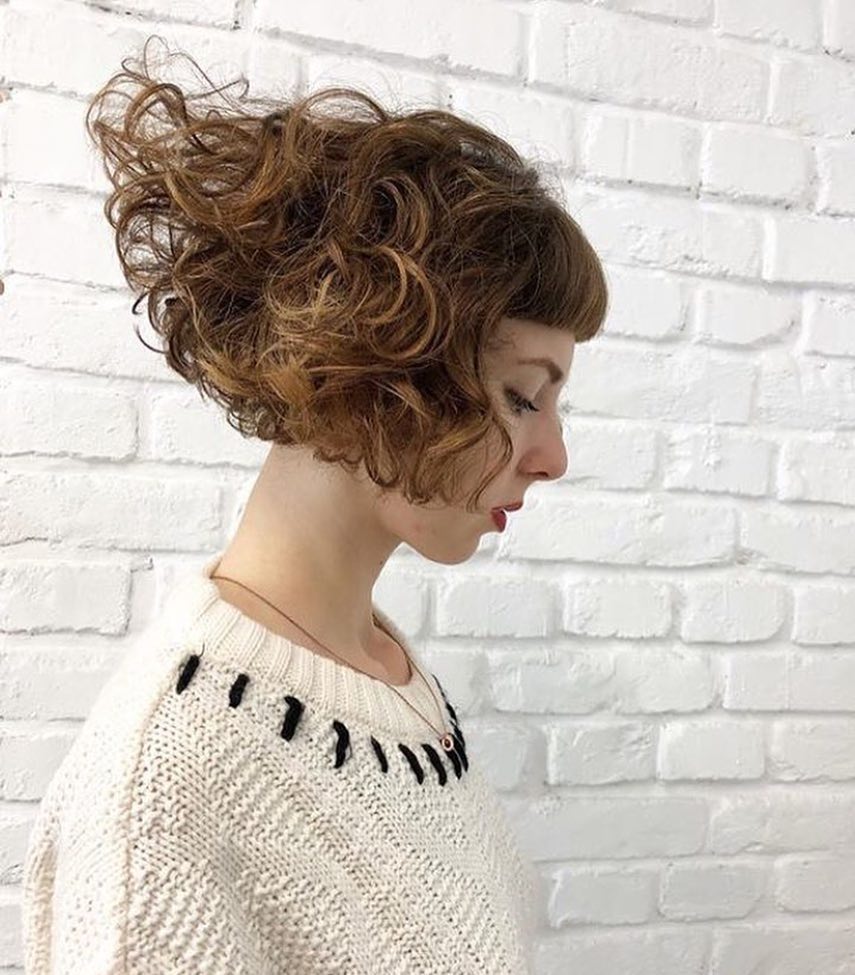 A curly stacked bob with caramel brown ringlets and short baby bangs.