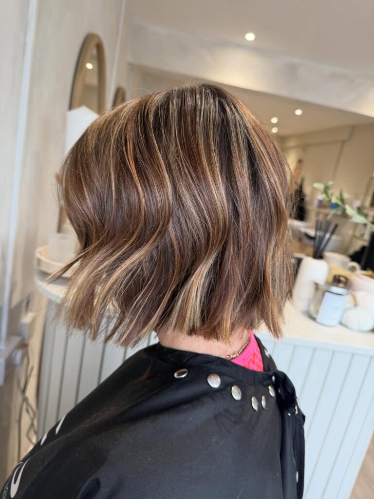 A side profile view of a woman with a chin-length choppy golden blonde bob featuring soft beachy waves and wispy face-framing bangs.