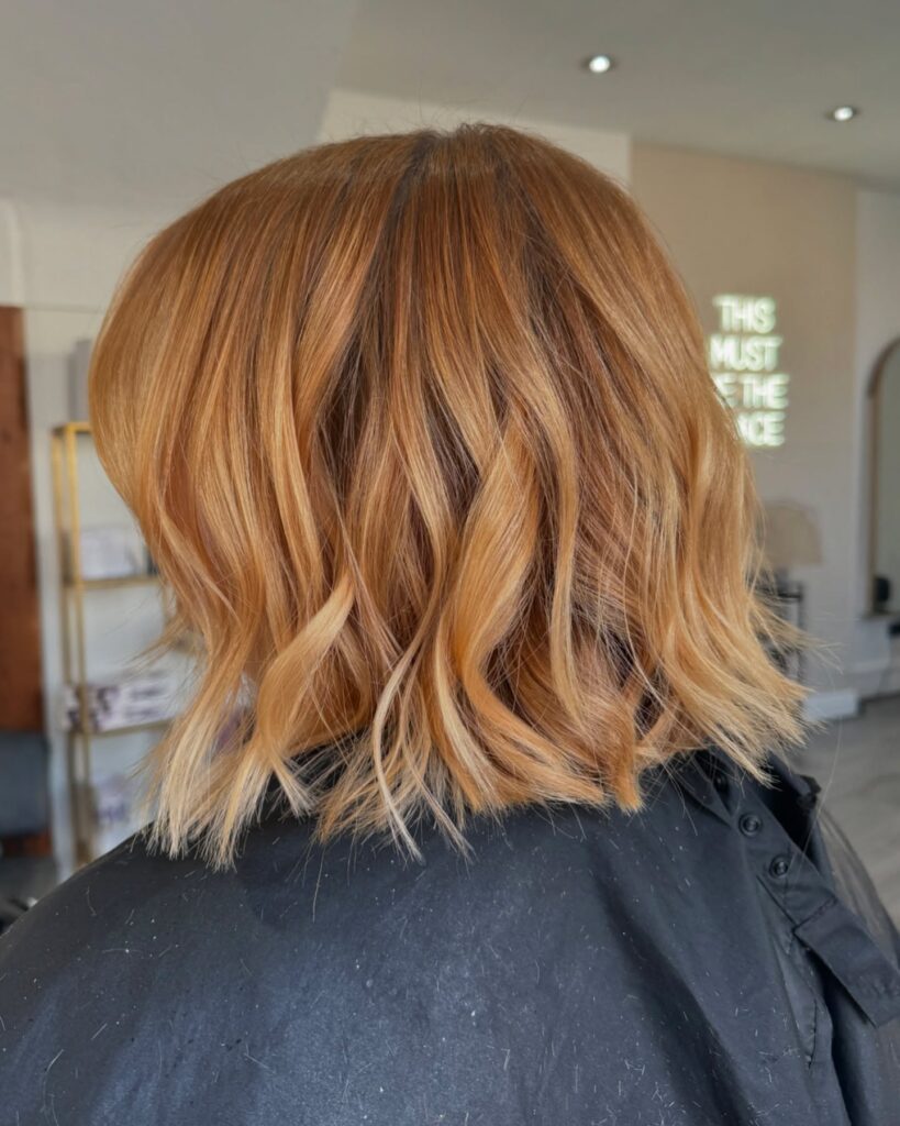 A woman with a jaw-length choppy copper bob featuring textured piecey layers and face-framing curtain bangs.