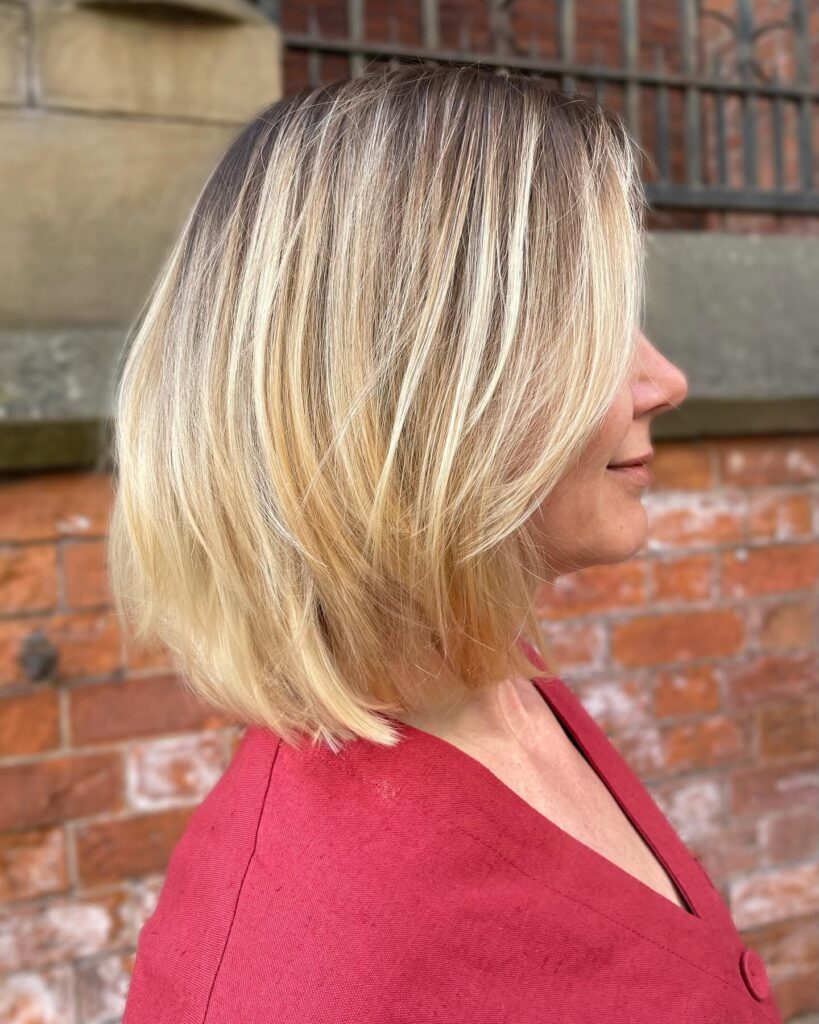 A side profile view of a woman with a chin-length choppy sandy blonde bob showing tousled waves and soft face-framing bangs.