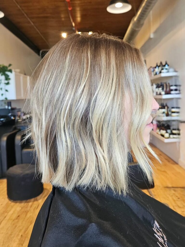 A woman showing a side view of a shoulder-length bright blonde choppy lob with blunt ends and piecey face-framing layers.