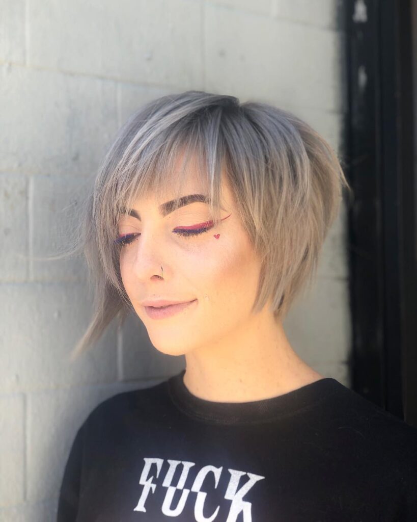 A woman with an asymmetrical short silver bob featuring choppy layers and wispy side swept bangs.