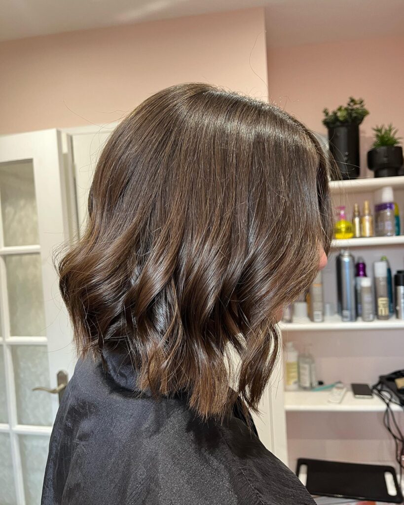 A side profile of a woman with a choppy chocolate brown bob styled in textured loose waves.