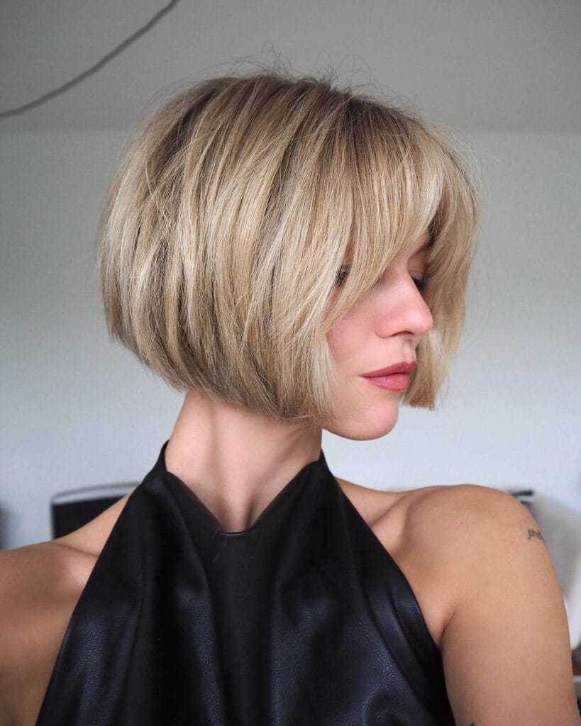 Voluminous blonde long bob with layered curtain bangs and soft textured movement.