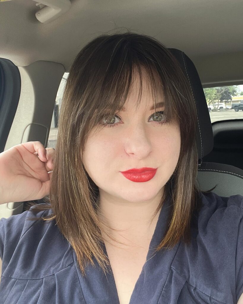 A woman with a sleek, straight, long brunette bob and thin, wispy bangs that graze her eyebrows.