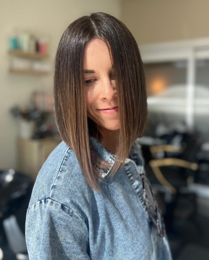 A woman showcasing a sleek inverted long bob in a rich mocha brown with an asymmetrical cut that is longer in the front.