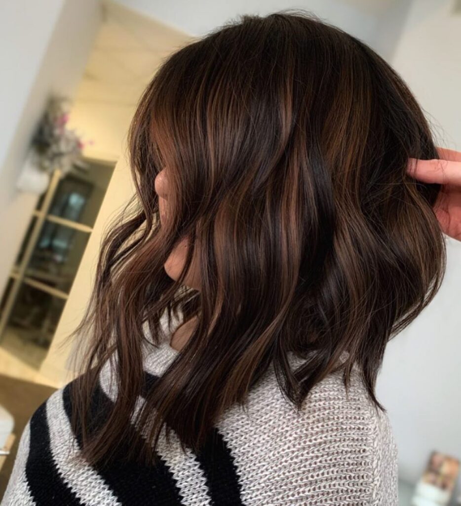 A side view of an angled brunette long bob with mahogany highlights and soft waves.