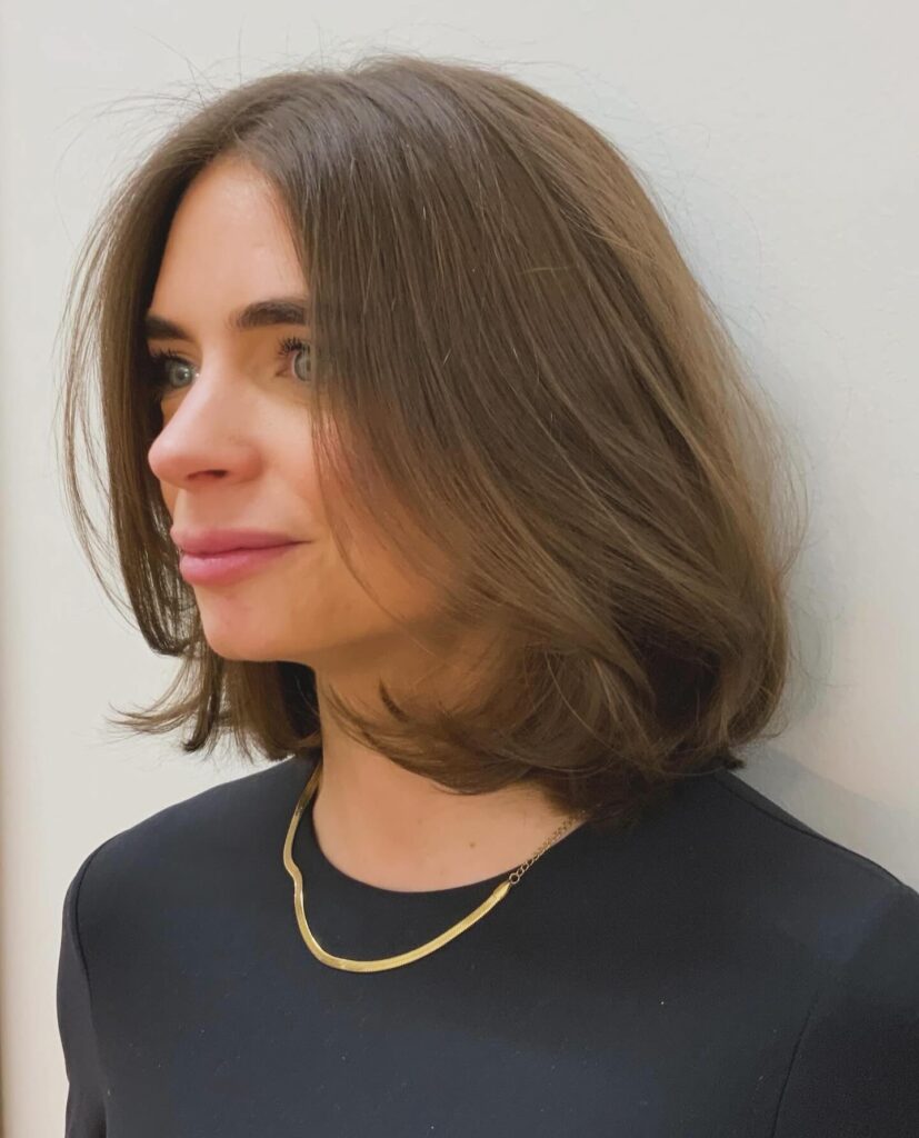 A woman with a soft, voluminous, mushroom-brown long bob featuring flipped-under ends and a middle part.