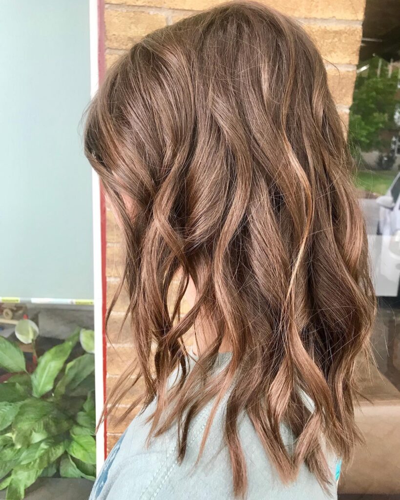 A woman from the back is showing a shoulder-length brunette lob with warm caramel highlights and piecey beachy waves.