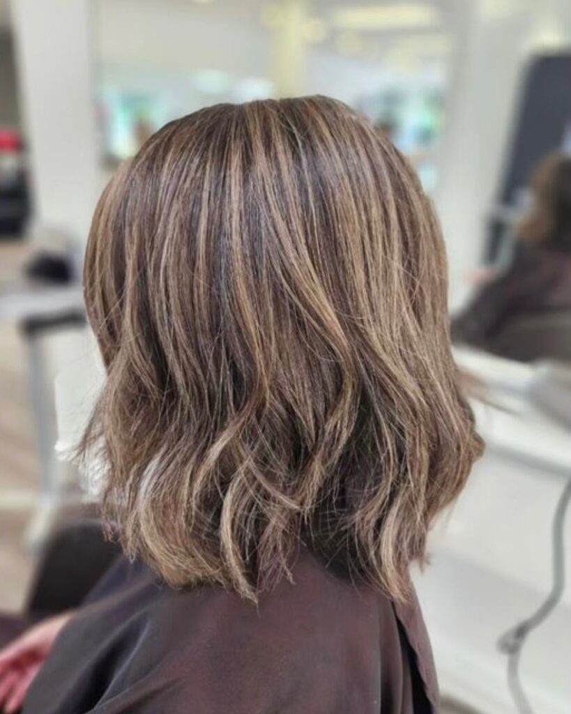 A back view of a woman with a textured long brunette bob featuring sandy blonde balayage and messy waves.