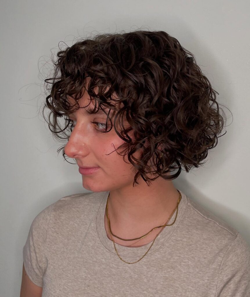 A woman with a dark brunette curly bob featuring short bangs and chin-length layered ringlets.