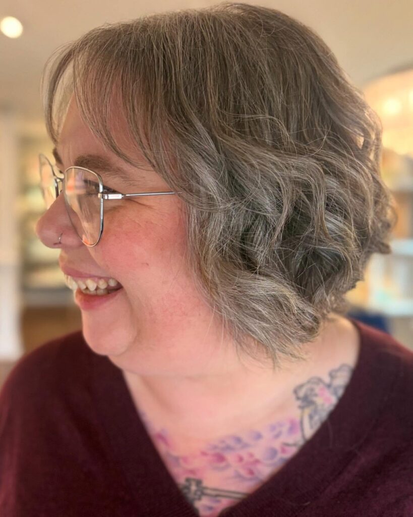A woman with a silver and gray wavy bob featuring light wispy bangs and chin-length layers.