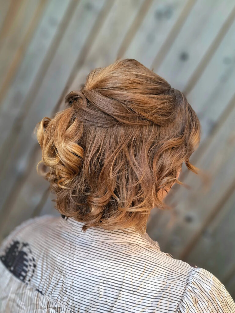 A woman with a neck-length curly bob featuring caramel highlights and a twisted half-updo style.