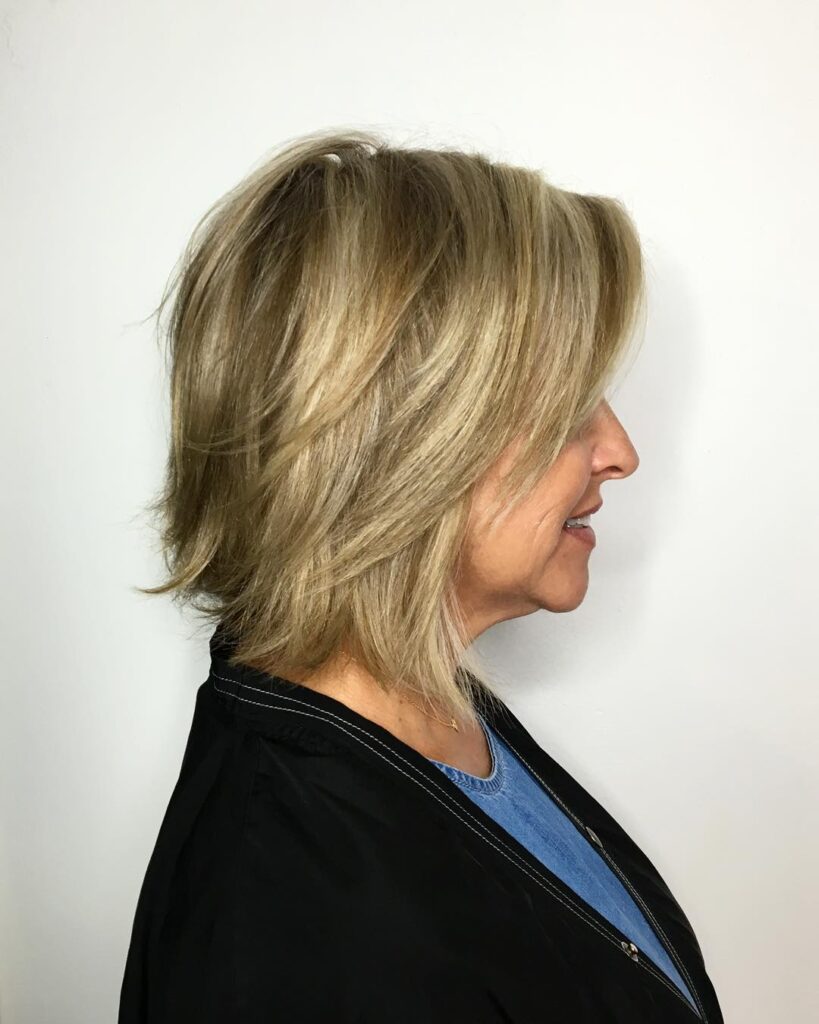 A side profile of a woman over sixty featuring a medium-length sandy blonde bob with choppy layers and textured ends.