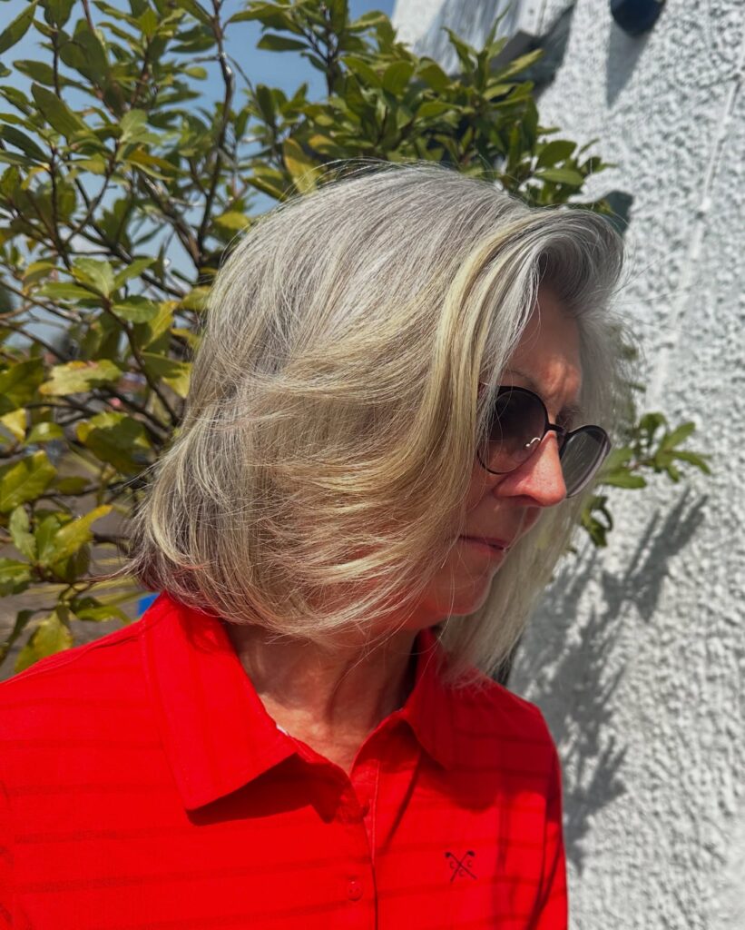 A woman outdoors wearing sunglasses with a chin-length choppy bob in silver and ash-blonde tones featuring swept-back layers.