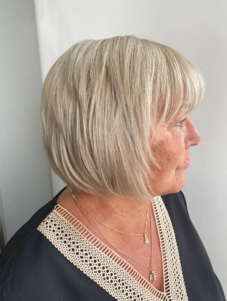 A woman in profile with a pearly platinum blonde bob featuring soft bangs and subtle choppy layers for added body.