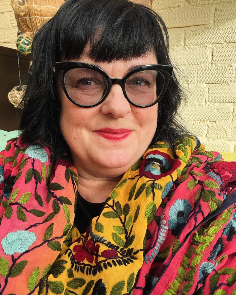 A woman over sixty with a jet-black choppy bob and thick straight-across bangs wearing cat-eye glasses.