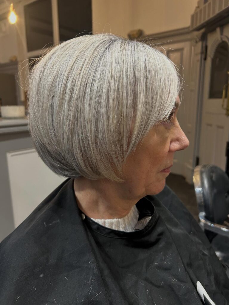 A woman in profile showcasing a sleek silver tapered bob with a rounded back and gentle side-swept layers.