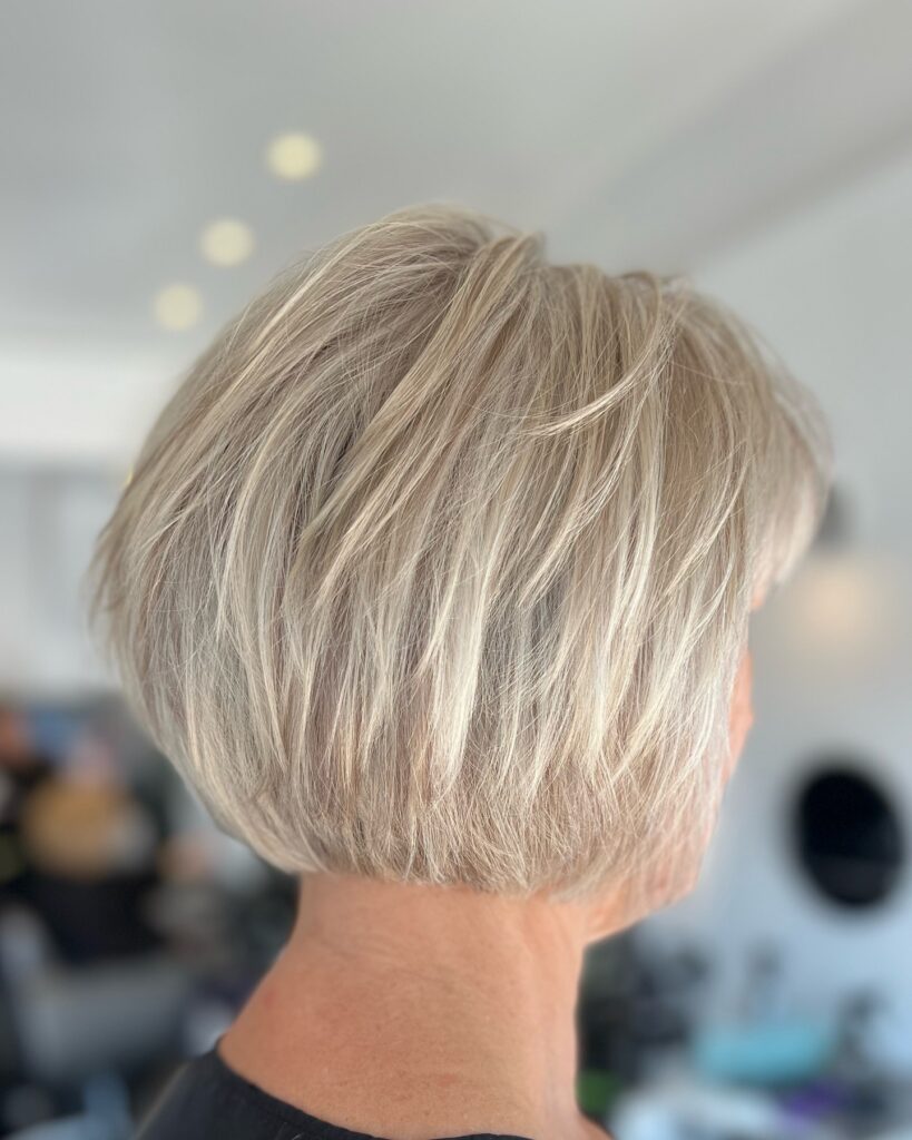 A back and side view of a woman over sixty with a champagne blonde graduated choppy bob featuring wispy layers.