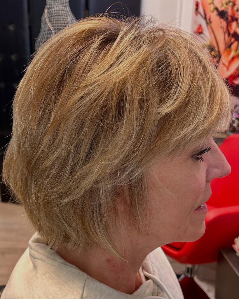 A side profile of a woman with a sandy blonde choppy bob featuring feathered layers and a soft side fringe.