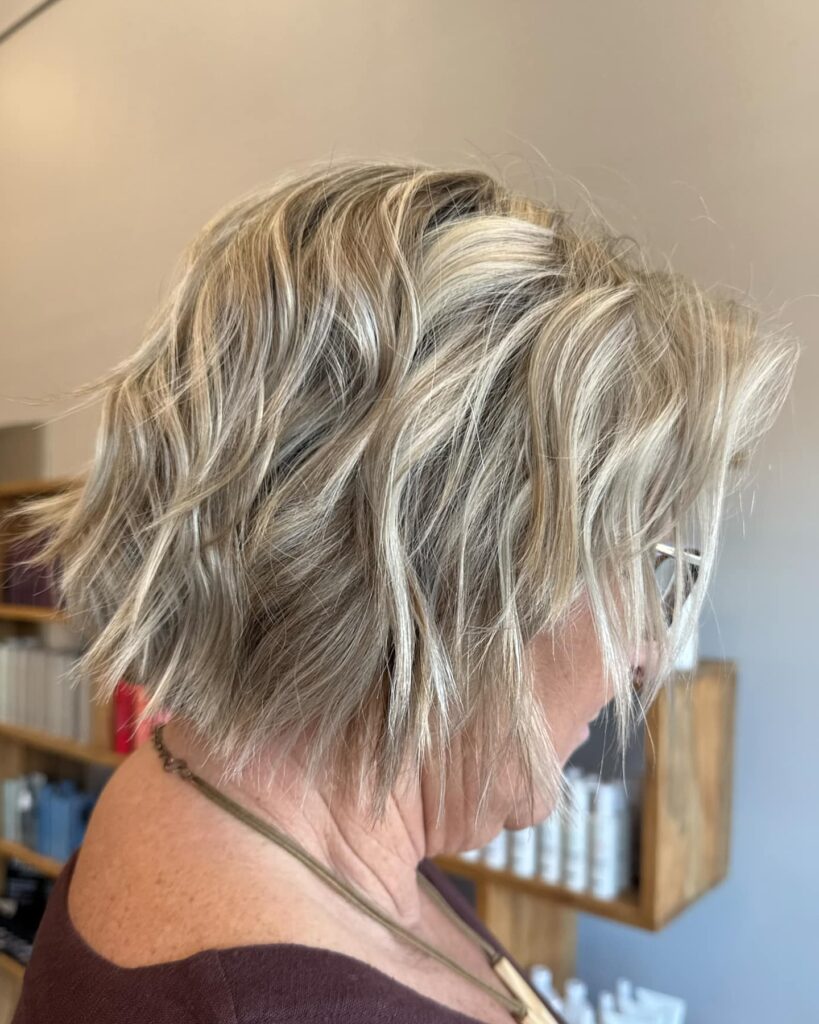 A side view of a woman with a choppy toffee blonde bob featuring heavily textured layers and messy beach waves.