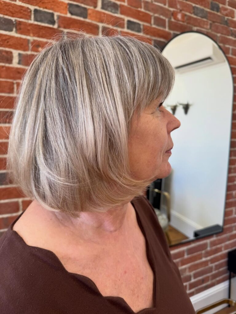 A side profile of a woman over sixty with a mushroom blonde bob featuring a soft fringe and gentle choppy layers at the ends.