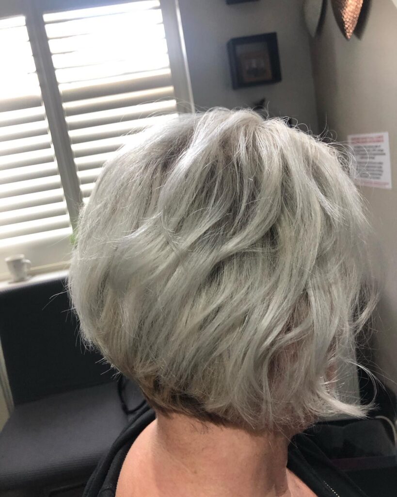 A back view of a woman with a short feathered silver bob featuring voluminous choppy layers and a tapered nape.