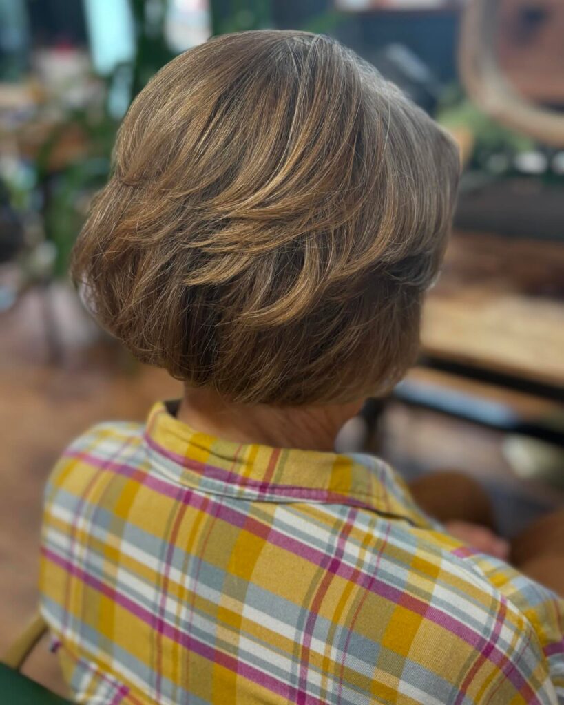 A back view of a woman with a stacked walnut brown bob featuring golden highlights and feathered layers.