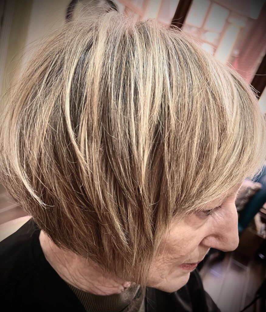 A close-up side profile of a woman over sixty with an ash-blonde choppy bob featuring fine feathered layers and wispy ends.