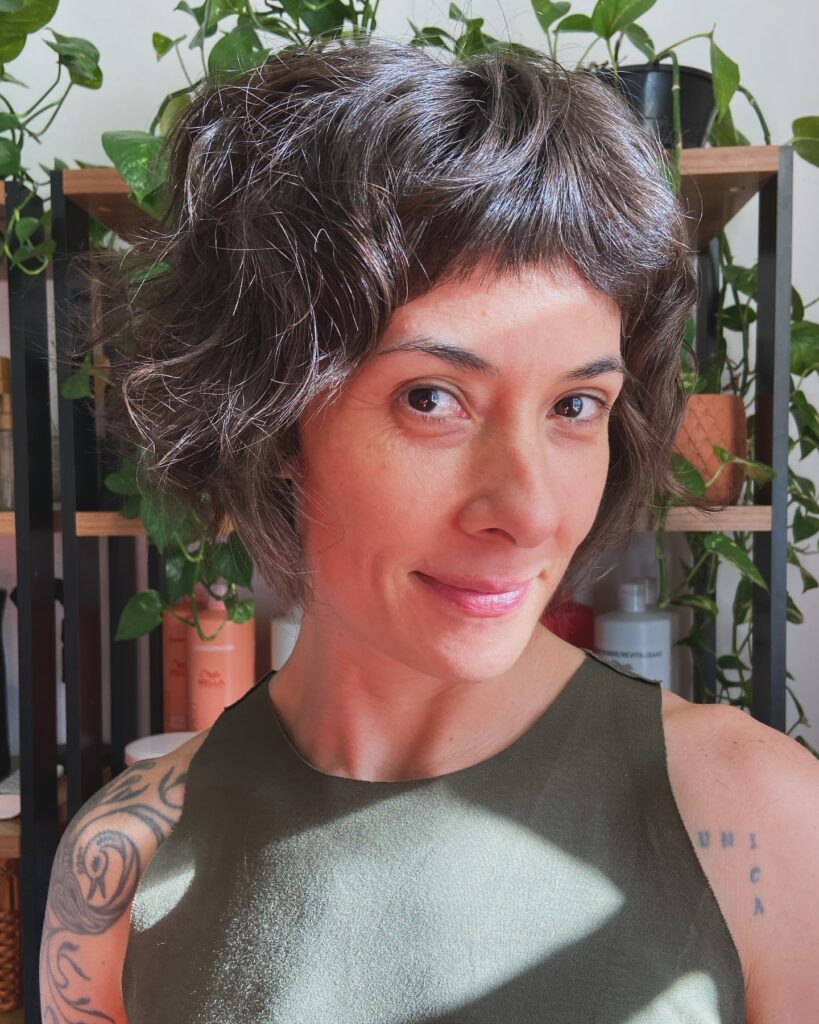 A front view of a smiling woman with a short, wavy espresso brunette French bob featuring choppy micro bangs.