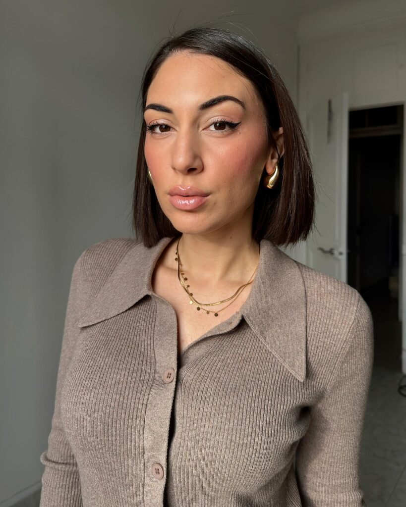 A front view of a woman with a sleek, straight, shoulder-length dark espresso brunette blunt bob with a side part.