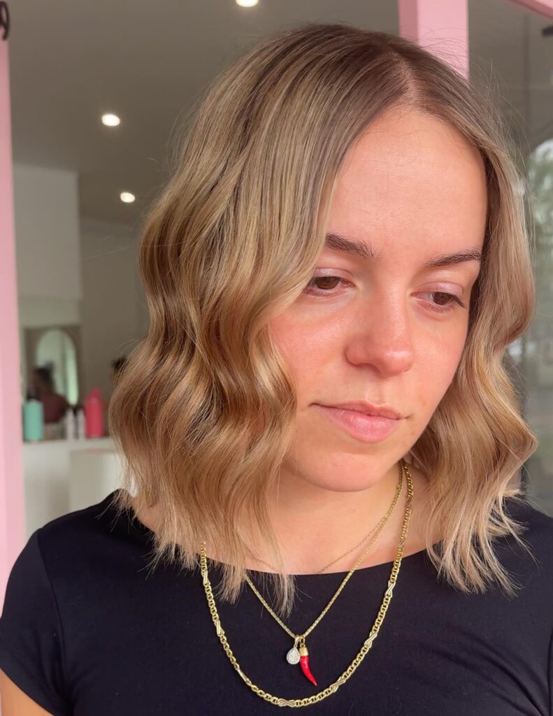 A woman looking down showcasing a shoulder-length golden blonde bob cut with a center part and soft uniform waves.