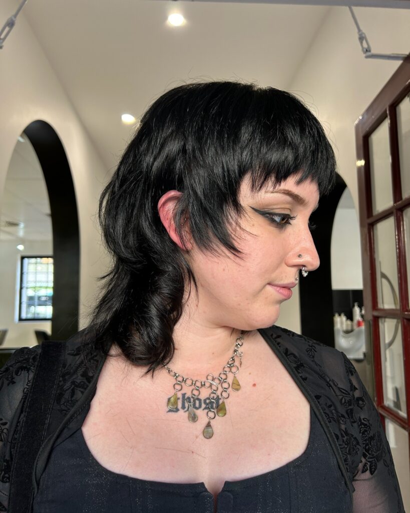 A side profile view shows a woman showcasing a glossy jet black wolf cut bob with razor-sharp layers and a textured full fringe.