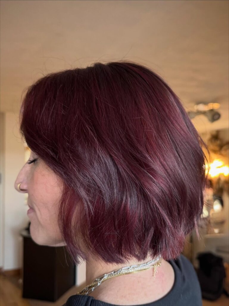 A woman showcases a chin-length deep burgundy choppy bob hairstyle with piecey texture and subtle layers.